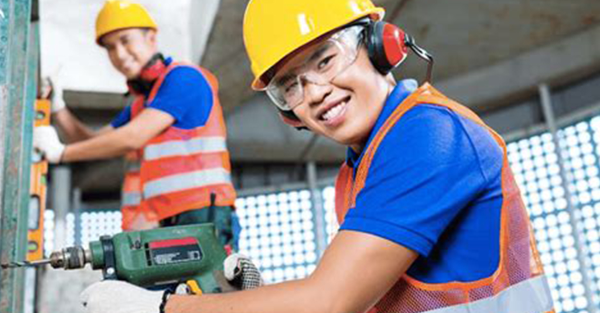 Young person wearing a hard hat and operating an electric drill